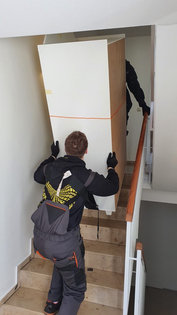 Mitarbeiter von Seniorenumzüge Lüneburg tragen einen Schrank durch ein Treppenhaus