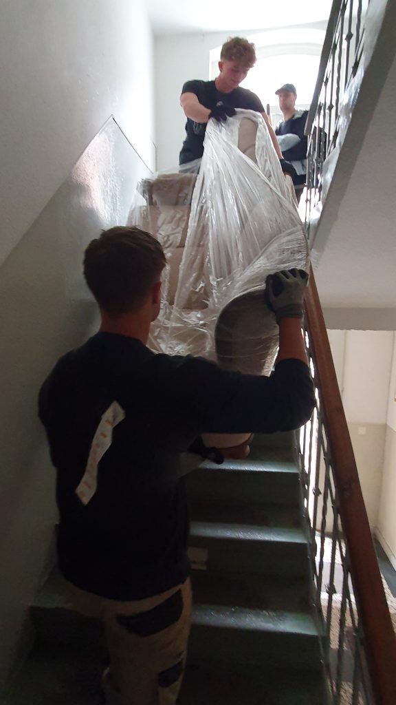 Umzugshelfer von Seniorenumzüge Lüneburg tragen Möbel durch ein Treppenhaus